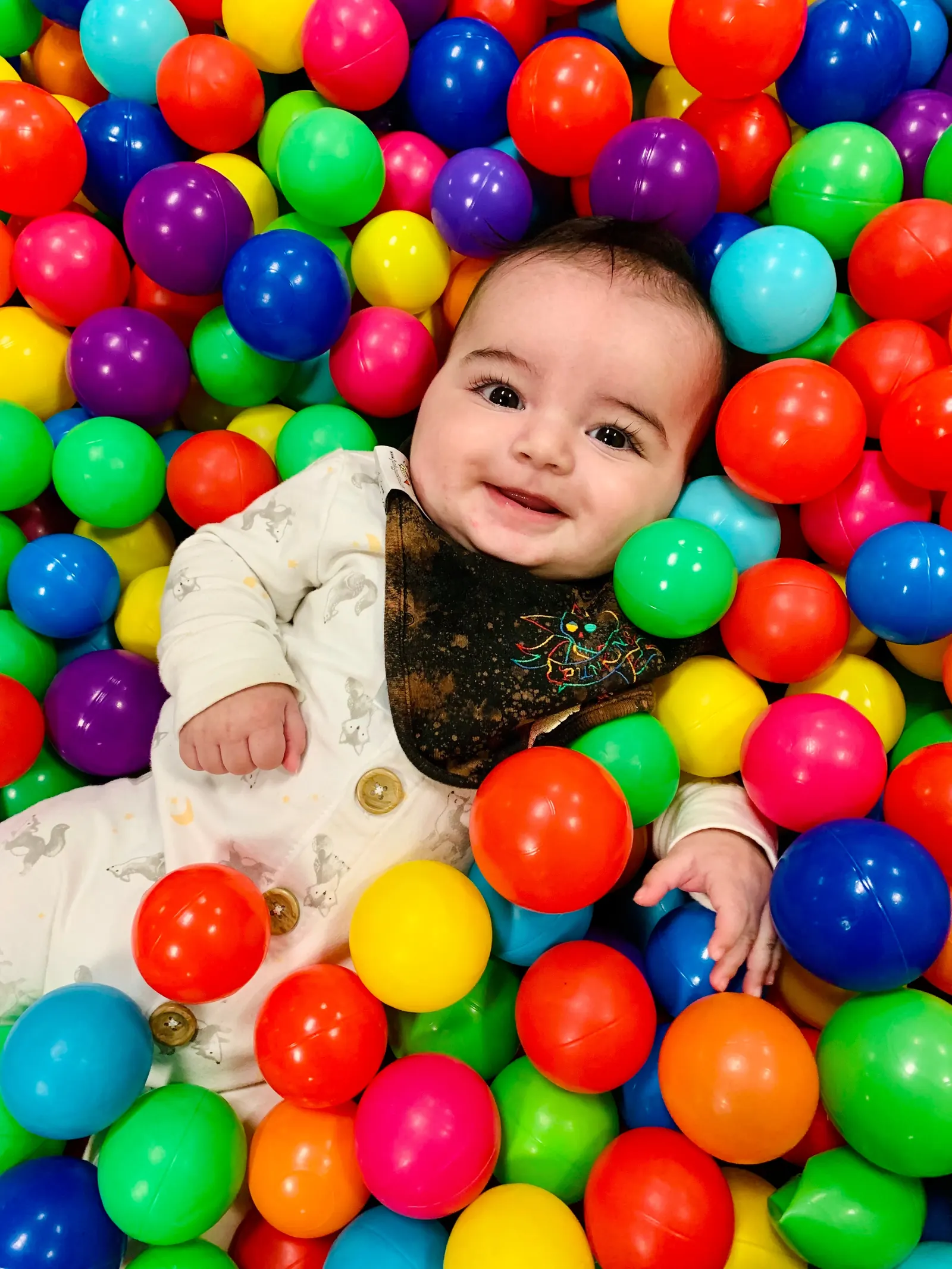 A smiling baby playing in Millie Moo's colorful ball pit